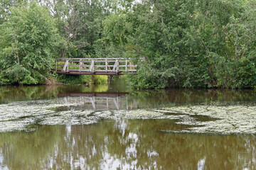 Summer view of a wooden pedestrian bridge over a small river.