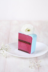 Slice of Wedding Mini Cake with chocolate gluten free sponge and blackcurrant mousse, covered with light blue fondant, decorated with fresh flowers, on a gray brick wall background.