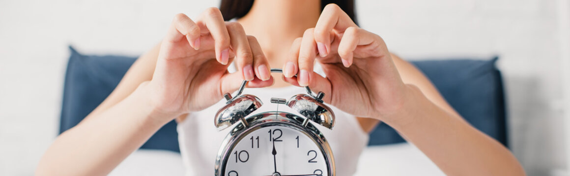 Horizontal crop of young woman holding alarm clock in bedroom