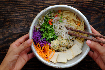 Homemade Vietnamese vegan noodles soup with colorful vegetables, people hand hold bowl to ready to eat
