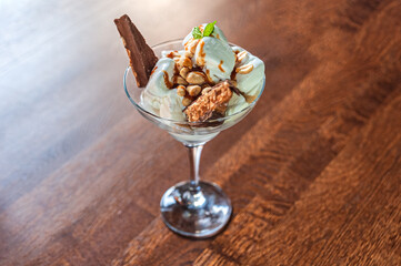 Dessert of white ice cream, peanuts and a chocolate bar with a mint leaf in a glass bowl on a wooden table