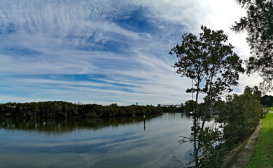 Beautiful view of a river with reflections trees, deep blue sky and rainbow look-alike clouds on water, Parramatta river, Rydalmere, Sydney, New South Wales, Australia
