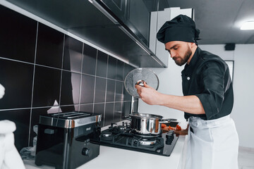 Professional young chef cook in uniform standing on the kitchen
