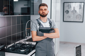 Young professional plumber in grey uniform standing on the kitchen