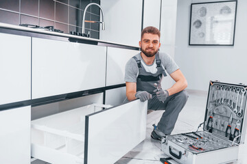 Young professional plumber in grey uniform using equipment on the kitchen and preparing for the work