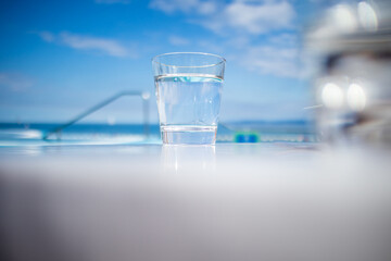 Glass of water standing near swimming pool in hot summer