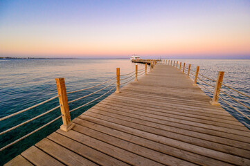 Fototapeta premium Wooden Pier on Red Sea in Hurghada at sunset and luxury yacht, View of the promenade boardwalk - Egypt, Africa