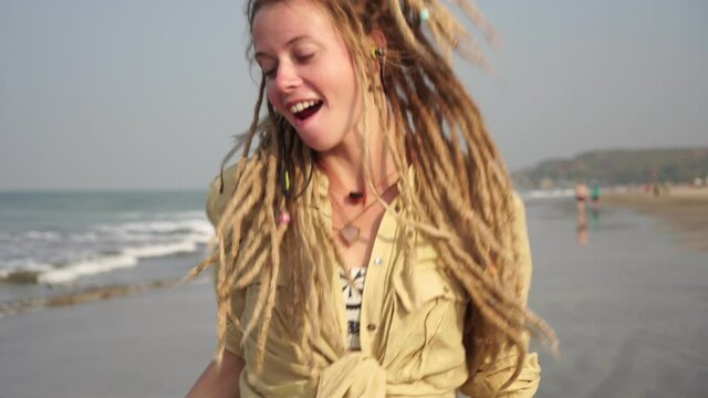 Cheerful woman with dreadlocks listens to music and dances on the beach.