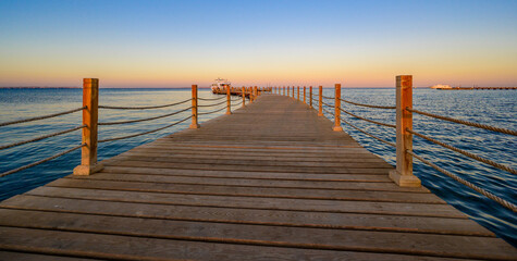 Fototapeta premium Wooden Pier on Red Sea in Hurghada at sunset and luxury yacht, View of the promenade boardwalk - Egypt, Africa