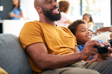 African American Father And Son Sitting On Sofa At Home Playing Video Game Together