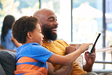 African American Family At Home With Father And Son Sitting On Sofa At Home Using Digital Tablet