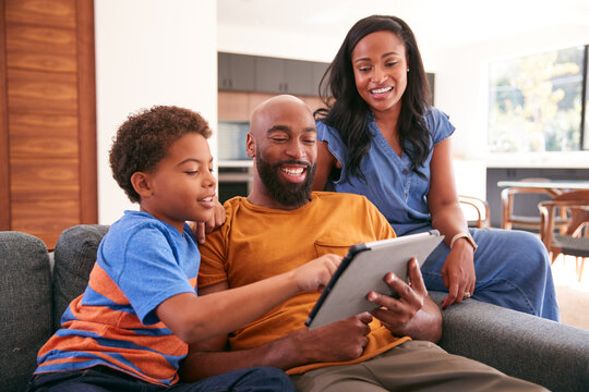 African American Family With Son Sitting On Sofa At Home Using Digital Tablet