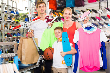 Young friendly parents with boy in school age shopping clothing in sport store. Focus on kid