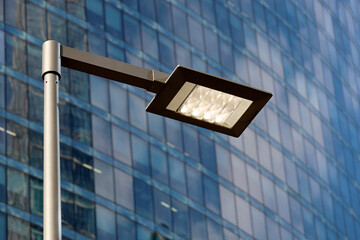 LED street lamp post glowing on skyscraper background. Modern led lights in city, saving of...