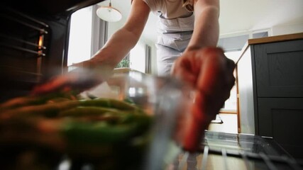culinary, food and people concept - woman cooking vegetables in baking dish in oven at home kitchen - Powered by Adobe