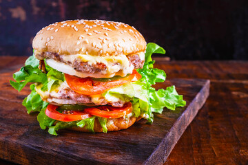 Close-up of delicious fresh home made burger with lettuce, cheese, onion and tomato on a rustic wooden plank on wooden table