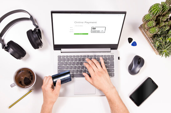 Online payments top view concept. Man is shopping online and paying with credit card. Desk flat lay view with laptop, mobile, coffee, headphones and mans hands.