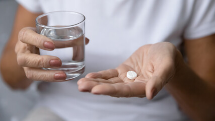 Close up mature woman hands hold pill and glass of natural clean water. Older generation female take analgetic painkiller drug. Painful old age, caring for health of senior citizen, daily meds concept