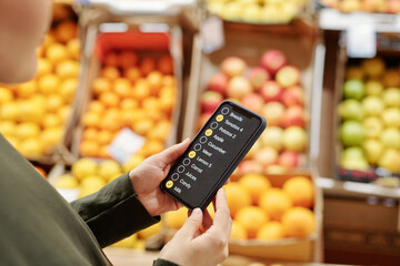 Over shoulder view of woman reading food product list on smartphone while making purchases at organic food market