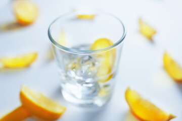 Out of focus glass filled with ice cubes and lemon slices, surrounded with slices of lemon