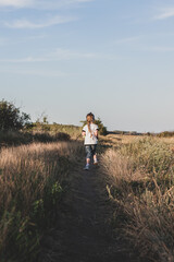 Adorable little girl with long braid running down the hill back view. Happy child running in wild grass countryside landscape. Family walking on fresh air. Local hiking travel concept.