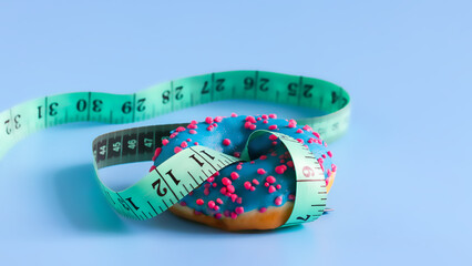 A sweet doughnut in blue glaze is intertwined with a centimeter measuring tape on a blue...