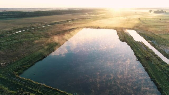Aerial drone shot of rising sun in the morning. Morning mist floating above the lake. Morning fog on the pond, sunrise shot. Golden rays of the sun paint the fog over the pond. Fishing holiday concept