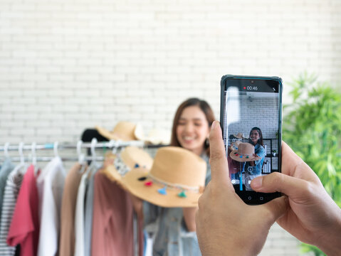 Asian Young Influencer Or Blogger Live Sell Summer Straw Hat And Record Video By Smartphone Vertical Style For Share Subscriber On Channel Or Social Media And Closeup Mobile Screen With Hand