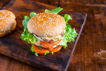 Close-up of delicious fresh home made burger with lettuce, cheese, onion and tomato on a rustic wooden plank on wooden table