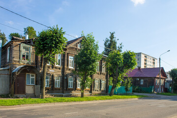 Old Kostroma street with wooden huts trees and a road on a summer day against a blue sky and space for copying