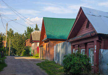 Old Kostroma street with wooden huts trees and a road on a summer day against a blue sky and space for copying