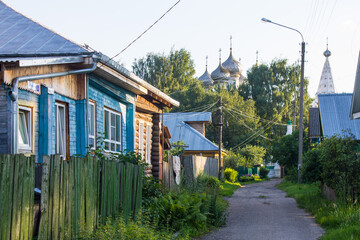 Fototapeta na wymiar Old Kostroma street with wooden huts trees and a road on a summer day against a blue sky and space for copying