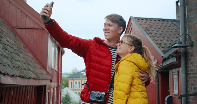 Couple of young tourists in centre of old European town or city. Make selfie photos on smartphone application. Happy staycation and exploring. Modern millennial conscious generation creating content