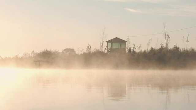 Rising sun in the morning over the pond. Morning mist floating above the lake. Morning fog on the pond, sunrise shot. Golden rays of the sun paint the fog over the pond. Fishing holiday concept