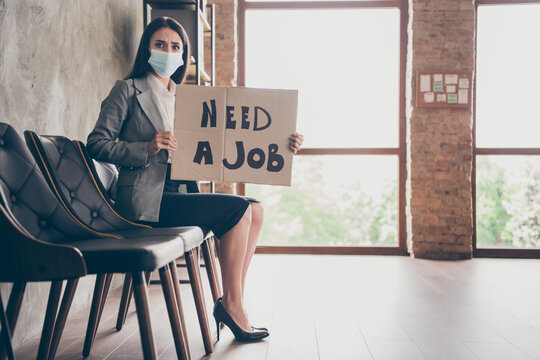 Full length profile side photo of scared girl marketer agent sit chair have job interview feel worry hold card board text wear blazer jacket high-heels medical mask in workplace workstation