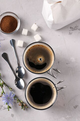 Chicory beverage in two glass cups, with concentrate and flowers on grey background. Healthy herbal beverage, coffee substitute, Vertical format, Top view