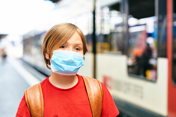 Young kid boy wearing face mask and backpack, standing at the train station, metro or bus station