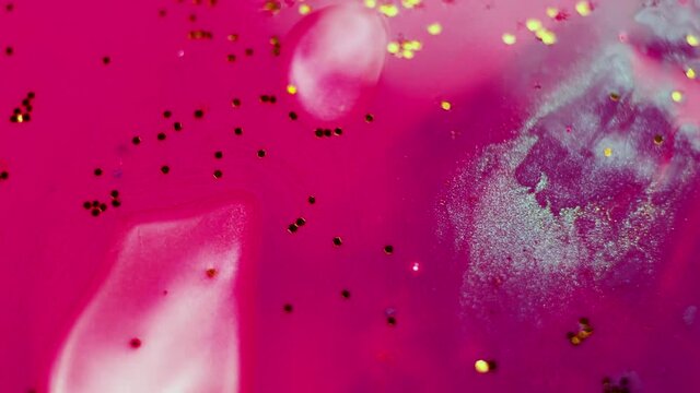 Abstract liquid pink background with gold glitter elements. Surface with a moving stream of paint and glitter, creative drop color
