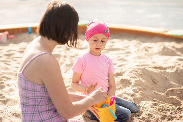 Small cute girl with mom share a sandcastle in a sandbox