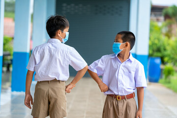 Asian children in school uniform wearing protective mask to Protect Against Covid-19 are shaking elbows greeting each other,Elbow greeting style,Coronavirus prevention,Social distancing.