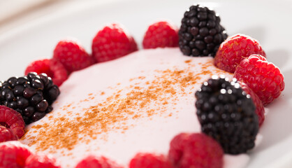 raspberries and blackberries laid out on a white plate in circle with yogurt and cinnamon