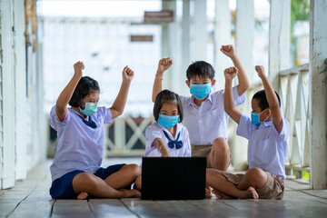 Group of students wearing protective mask to Protect Against Covid-19 use laptop to have online class happily at Thailand school classroom.
