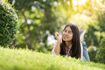 Naklejka na ściany i meble Relax beautiful asian woman smiling face Lying down on green grass field in outdoors garden park enjoy nature morning. Freedom Lifestyle woman breathing fresh air in green park on spring lawn outdoors