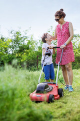 Mother and boy talking and laughing while mowing grass with lawn mower