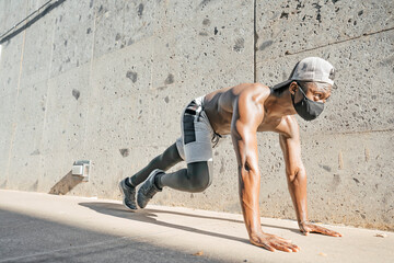 Athletic black man is training in urban area while wearing a mask.