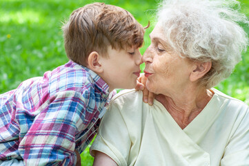 Grandmother with her grandson face to face in an embrace summer. Emotional portrait close up. The grandson kisses his grandmother. Family values, love, trust, relationships