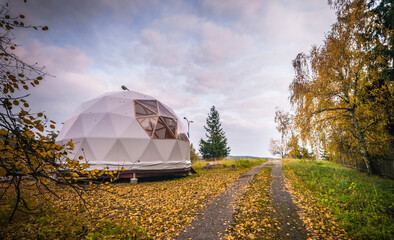 Large geodesic dome tent in autumn forest. Modern outdoor glamping tent on meadow.