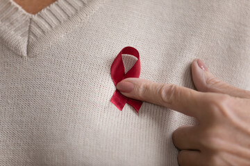 Close up old female hold red ribbon on breast to raise awareness support of AIDS or human immunodeficiency virus. Universal symbol of stop drug abuse. World AIDS Day. Regular checkup promotion concept