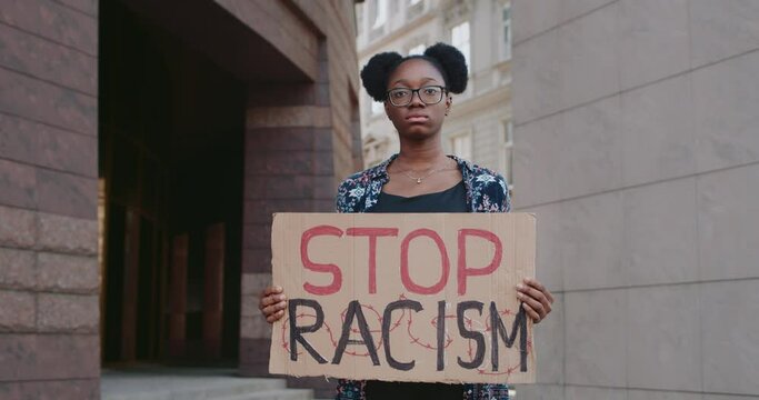African american girl supporting anti racism campaign at city street.Young femalestudent holding cardboard with stop racism phrase . Concept of equal human rights and tolerance