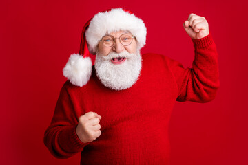 Yeah x-mas discounts. Ecstatic old retired man pensioner in santa claus headwear raise fists enjoy tradition fairy greeting holiday wear bright jumper isolated shine color background
